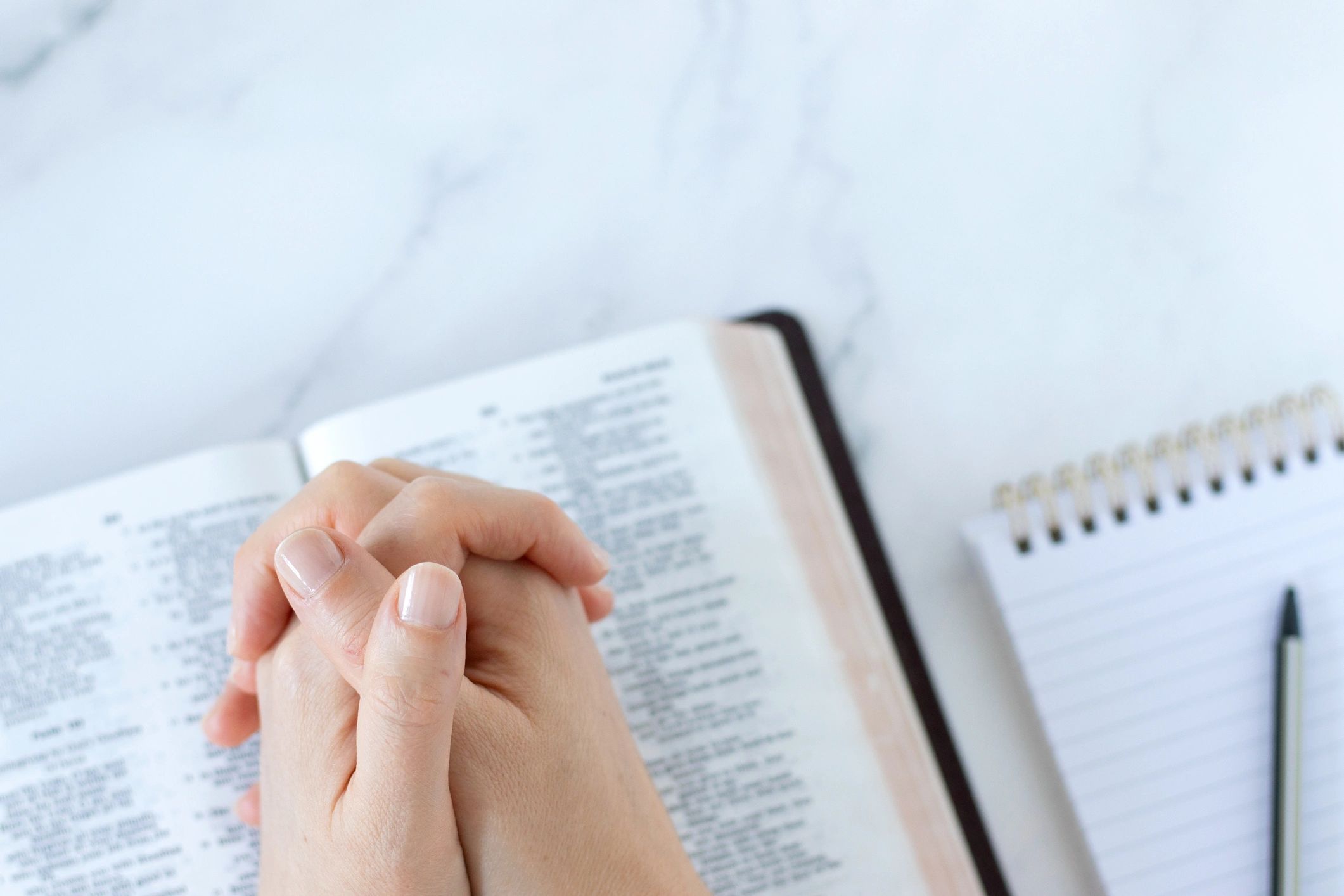Praying hands on top of open Bible book