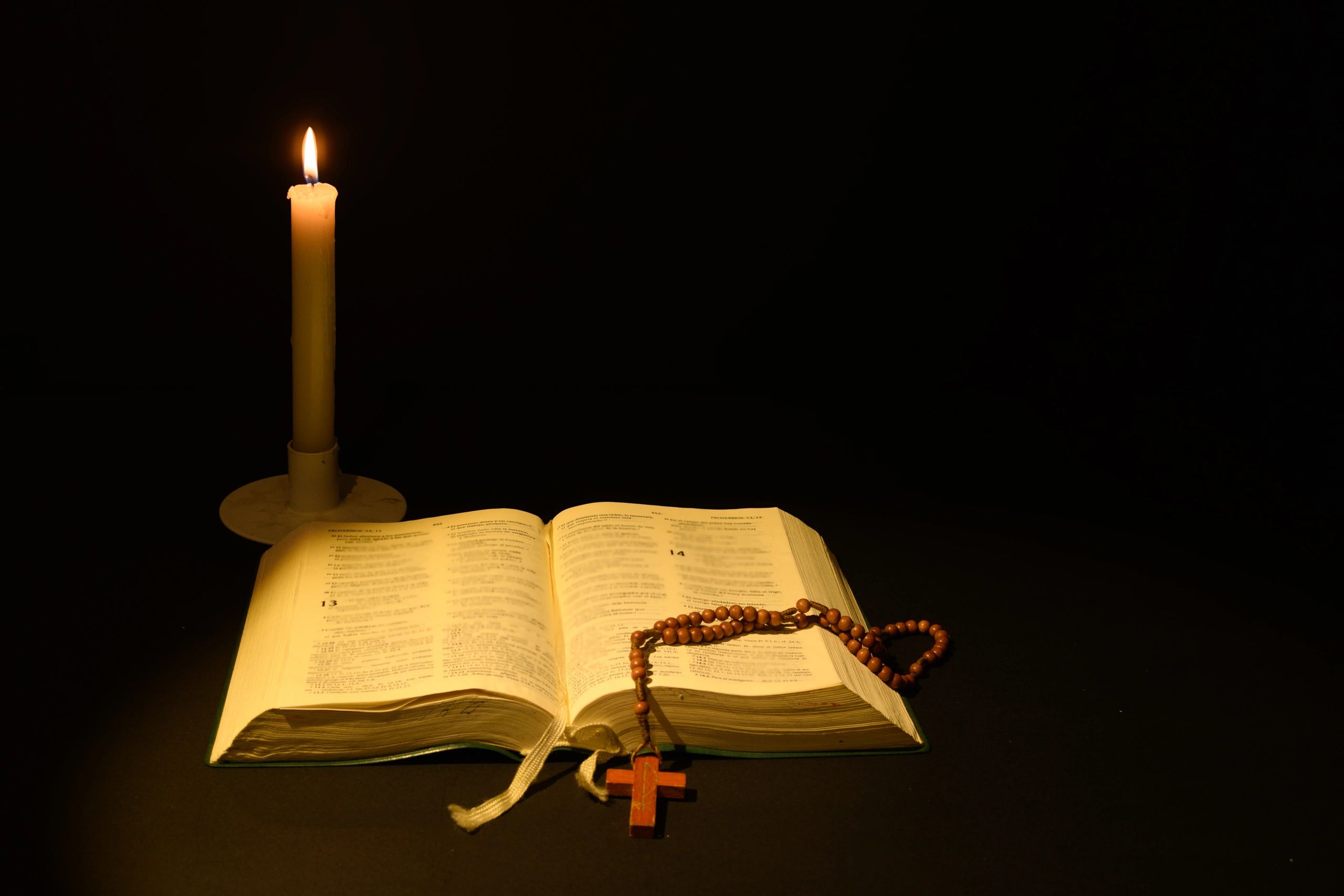 Candle beside an open Bible in a calm dark setting