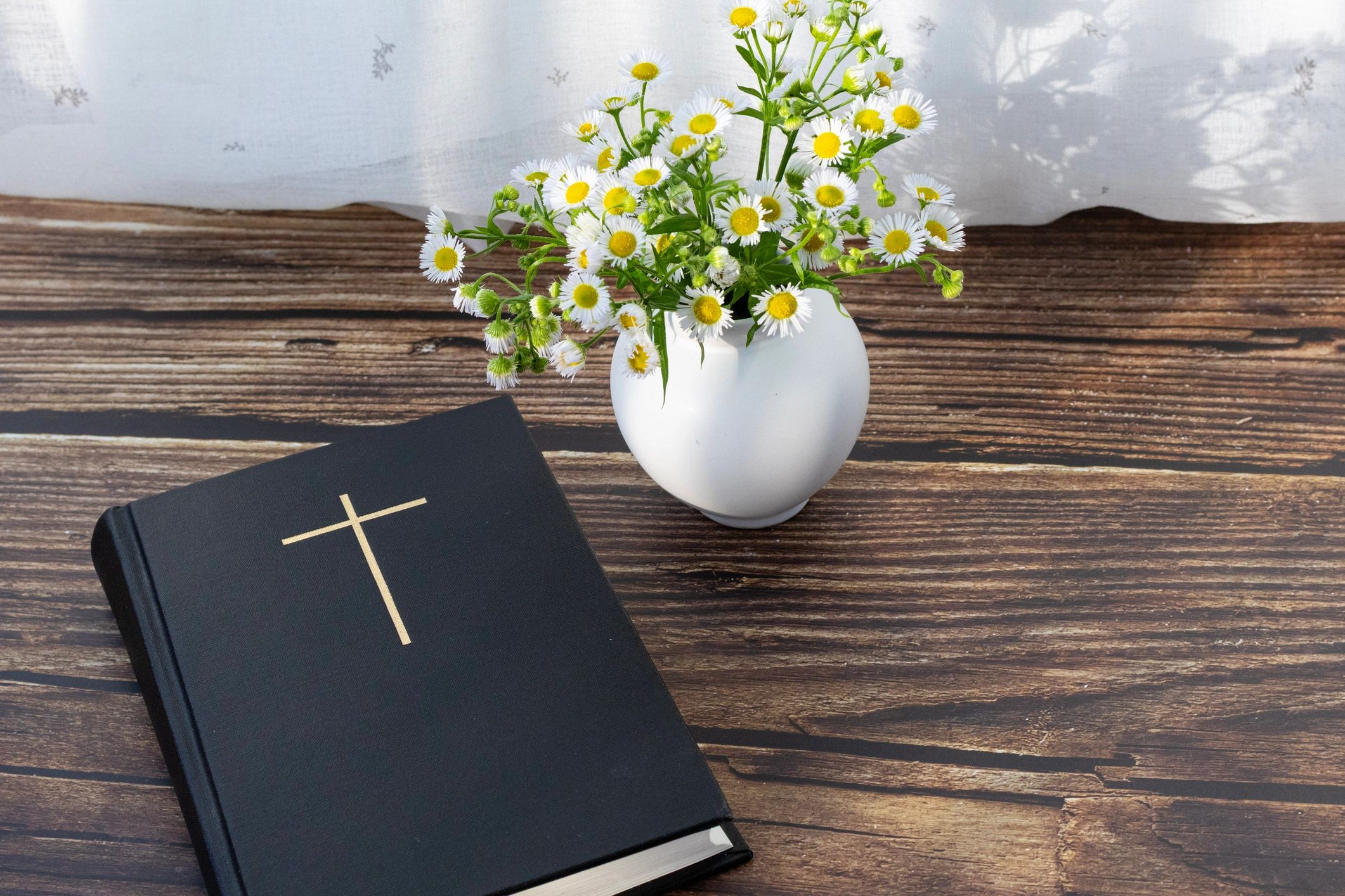 Open Christian journal with wooden cross symbol and wildflowers in soft morning light